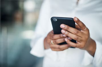 Cropped shot of an unrecognizable businesswoman standing alone in the office and using her cellphone during the day