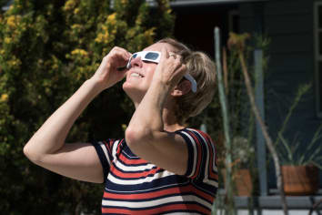 woman in striped shirt watching eclipse with glasses