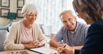 Two seniors sitting at table smiling during consultation with business woman