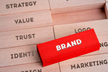 A red wooden piece that says Brand laying on top of other natural wooden pieces that say strategy, value, trust, identity, logo, and marketing. 