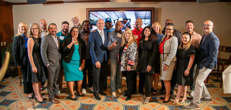 Members of BBB Heart of Texas and NFL Alumni standing side-by-side smiling in a meeting room.