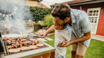 A father teaches his son how to cook hamburgers and hot dogs on a backyard grill.