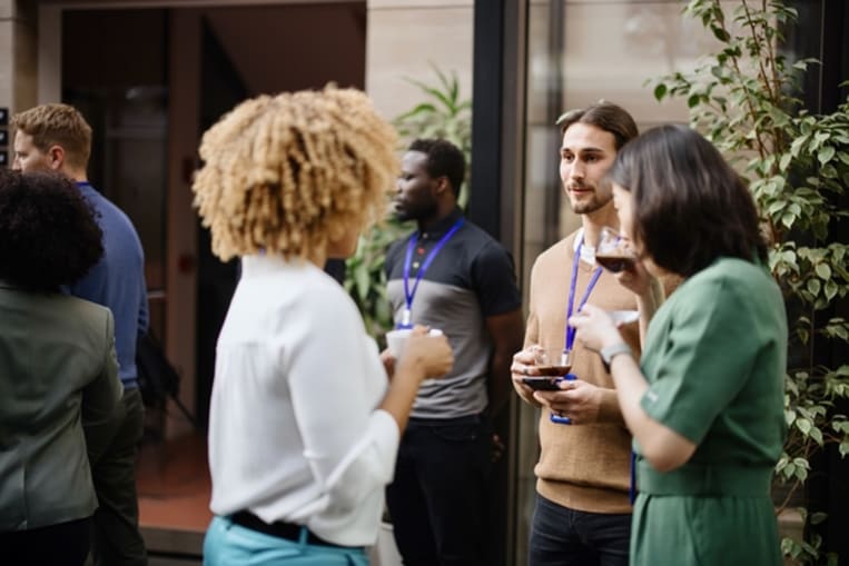 Image of two young women standing and drinking coffee networking with another young man.