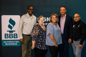 BBB staff members pose for a photo in front of a BBB branded backdrop