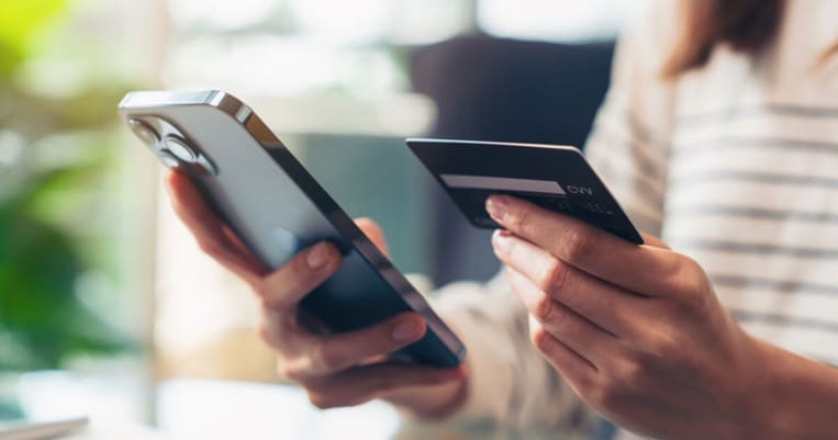 Person holding cell phone in one hand and credit card in other hand making payment