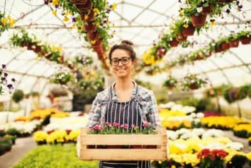 woman in greenhouse holding crate of plants