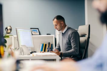 A man in professional attire is calculating finances in front of a computer.