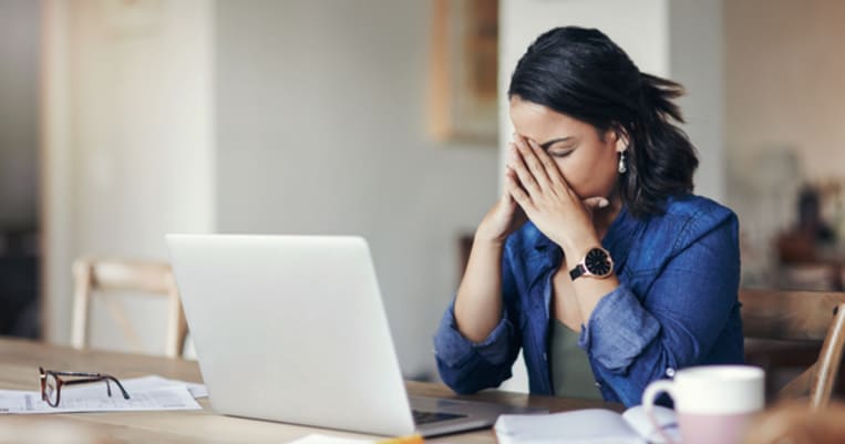 Upset woman hands on her head with laptop in front of her