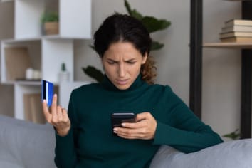 Concerned woman looking on smartphone having issues with credit card