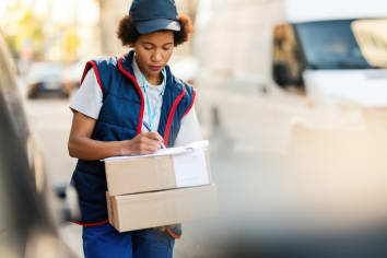 Black female courier writing down the address while delivering packages in the city. 