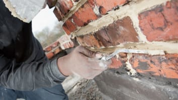 Close-up on a mason smoothing a mortar joint on a brick chimney.