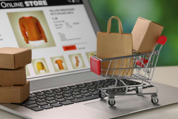 Mini shopping bag, boxes and cart on laptop, closeup. Online store