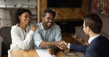 Happy couple smiling and shaking the hand of insurer