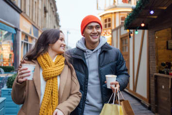 Couple shopping for the holidays dressed in winter gear and holding coffee and holiday bags on a city street