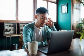 Man with his hand on head, using laptop computer at home