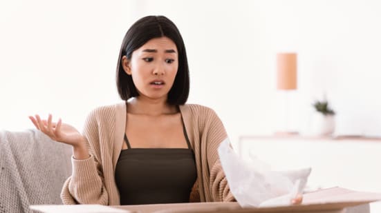 Wrong Item Concept. Dissatisfied unhappy asian woman sitting on sofa with cardboard box, received parcel with wrong or damaged staff, spreading hands in disappointment, feeling upset with bad purchase (Wrong Item Concept. Dissatisfied unhappy asian wo