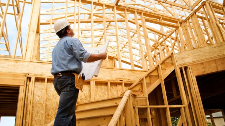 A worker wearing a hard hat inspects a home construction site.