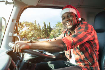 Smile Confidence truck driver wear Santa Clause hat driving semi-truck In Business Long transport. Trucker lifestyle young man African American working holidays. Merry Christmas and happy new year.