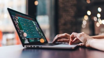 Close-up on a laptop screen and hands on the keyboard. The laptop is showing an online poker game.