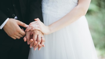 A close-up on a newlywed couple wearing a tux and bridal gown. They are holding hands and wearing wedding rings.