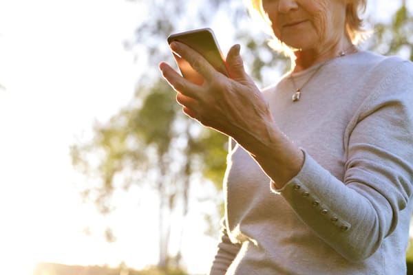 Elderly woman is holding a phone in a sunny park. Show care and love for the elderly, help charitable foundations. Be careful on the Internet, fraud (Elderly woman is holding a phone in a sunny park. Show care and love for the elderly, help charitable
