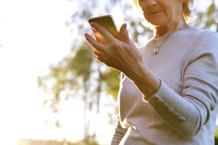 Elderly woman is holding a phone in a sunny park. Show care and love for the elderly, help charitable foundations. Be careful on the Internet, fraud (Elderly woman is holding a phone in a sunny park. Show care and love for the elderly, help charitable