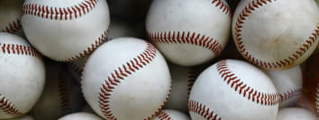 Close-up shot of several baseballs clustered together, showing the white leather and red stitching.