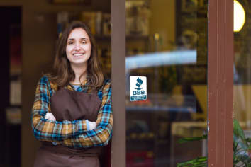 Female business owner in front of storefront with BBB Accreditation Seal. 