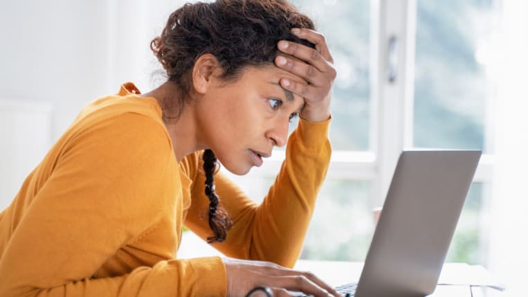 A stressed, concerned-looking woman leans over a laptop.