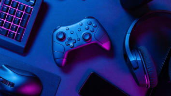 A video game controller sits alongside headphones, a keyboard, and a computer mouse in dramatic purple lighting.