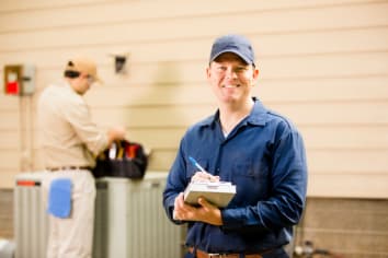 Air conditioner repairmen work on home unit. Blue collar workers.