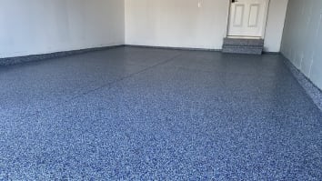 An empty home garage with blue speckled epoxy flooring installed.