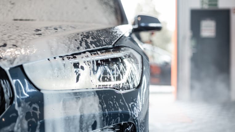 A close-up shot of a car's soapy front headlight as it moves through an automatic car wash.