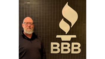 Hugh Grant, Region Director for BBB Ottawa, stands next to a wall with the BBB torch logo.