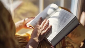 A close up on someone reading a book while sitting in a windowsill. The book is open to a page in the middle.