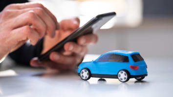 Concept photo for buying a car online: A closeup on someone typing on a cell phone with a small blue model car in the foreground.