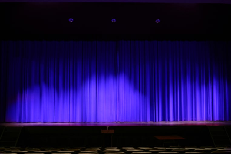 Theater stage with red velvet curtains and empty chairs in the foreground