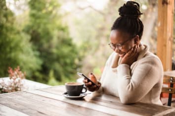 happy african woman smiling at phone at coffee shop