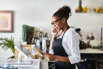 A friendly waitress taking order on phone at smoothie shop and writing on notepad