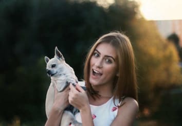 woman holding small dog in hand with surprised look on her face