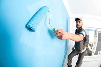 man painting a white wall with blue paint