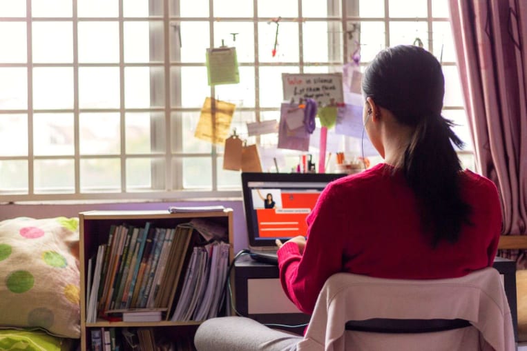 young woman looking at computer screen from desk in bedroom