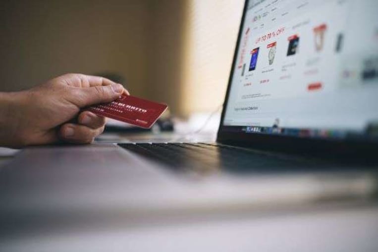 person shopping online with red credit card and laptop