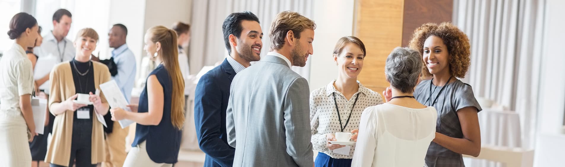 Professionals don lanyards with name tags at a conference as they introduce themselves and make small talk over coffee.