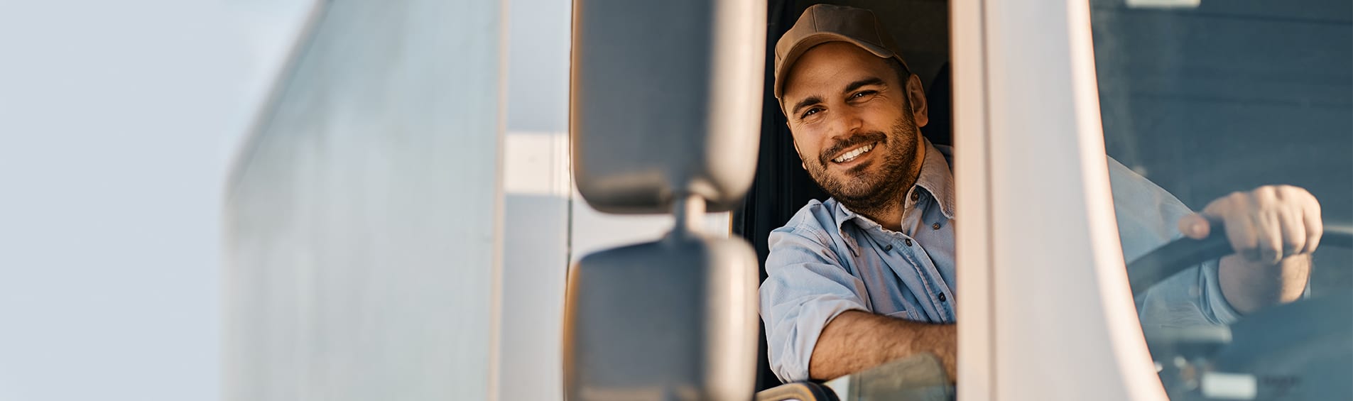 A gruff, bearded driver leaning out of his truck window smiling, with one hand on the steering wheel.